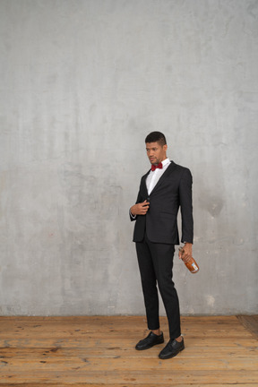 Young man in suit standing with a champagne bottle in his hand