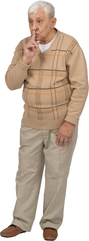 Vista frontale di un uomo anziano in abiti casual che mostra il segno del silenzio