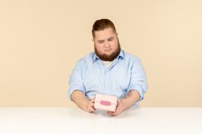 Grande homem sentado à mesa e segurando a lancheira