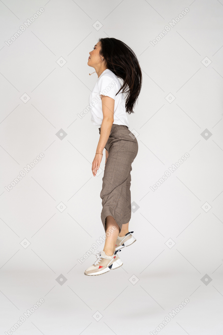 Vista lateral de una señorita saltando en calzones y camiseta extendiendo sus piernas