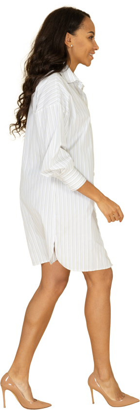 Vista laterale di una giovane femmina sorridente di carnagione scura a piedi in abito bianco