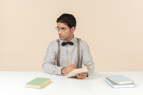 Man sitting at table with books and writing something in notebook