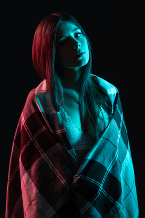 Close-up a young female standing in the neon lights wrapped in plaid