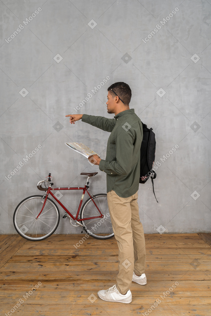 Three-quarter back view of a man with a backpack holding a map and pointing forward