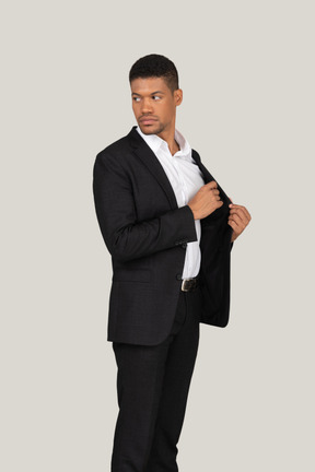 Side view of a young man in black suit putting something in pocket