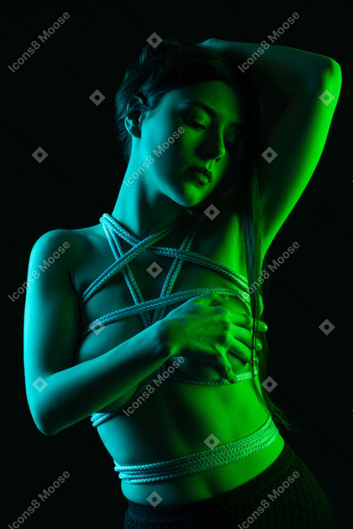 A sensual shot of a woman in harness posing under green light
