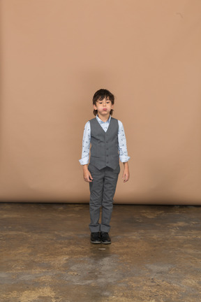 Vista frontal de un chico lindo en traje gris hinchando las mejillas