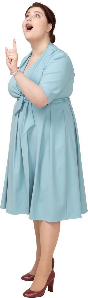 Vista lateral de una mujer en vestido azul apuntando hacia arriba con un dedo