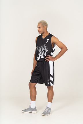 Vista de tres cuartos de un joven jugador de baloncesto masculino poniendo la mano en la cadera y mirando a un lado