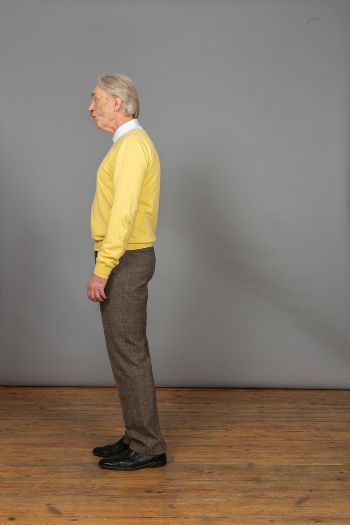Side view of an old surprised man in yellow pullover looking aside and grimacing