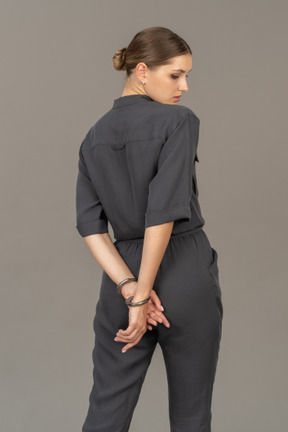 Three-quarter back view of a young woman in a jumpsuit wearing handcuffs