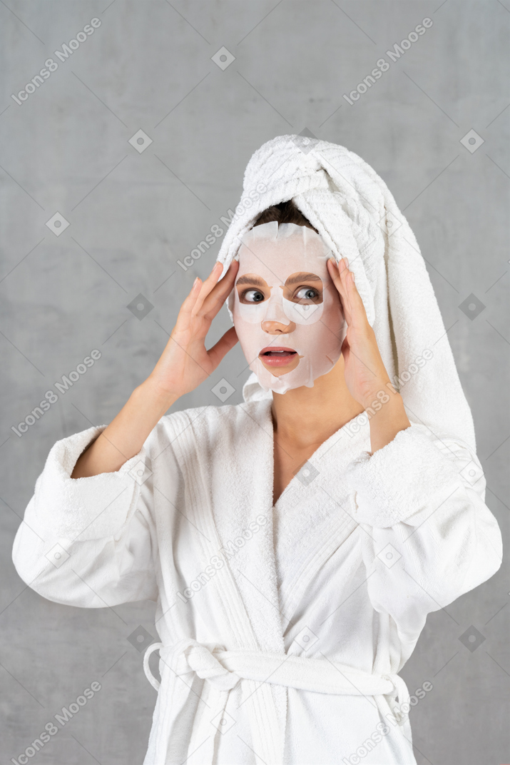Woman in bathrobe looking surprised and touching temples