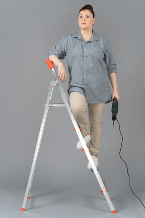 Young woman standing on stepladder with a drill