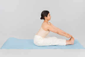 Young indian woman sitting on yoga mat and touching toes with hands