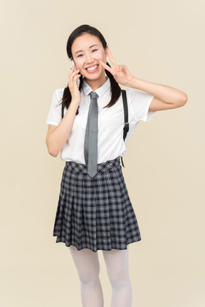 Asian school girl talking on the phone and showing v sign