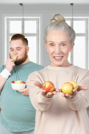 A woman holding apples and a man eating a salad