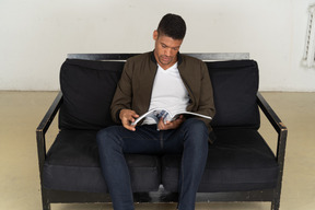 Beautiful young man sitting on a sofa and holding a magazine