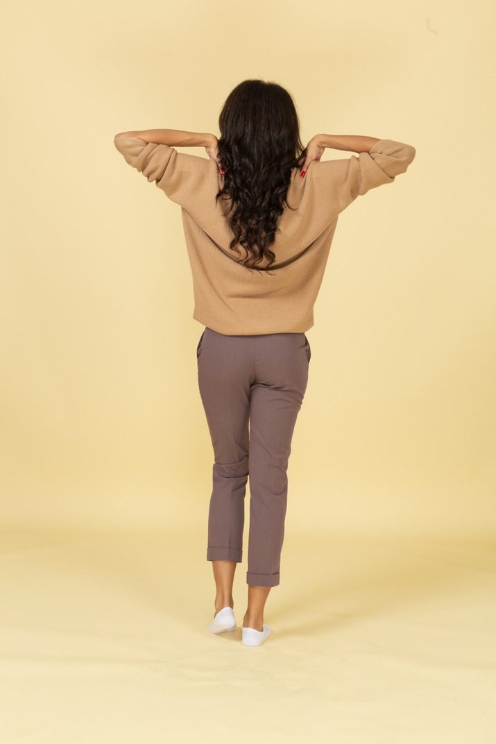 Back view of a dark-skinned young female touching her shoulders