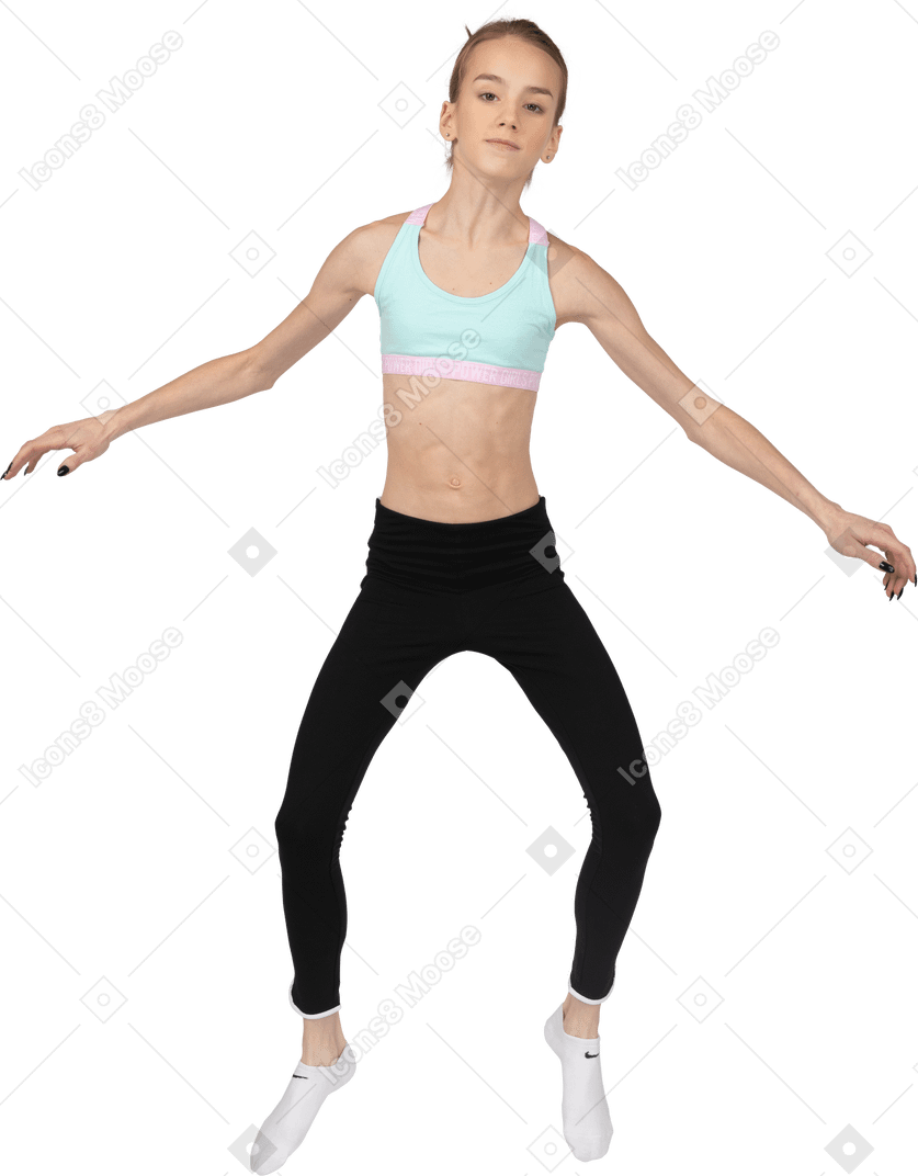 Vista frontal de uma adolescente em roupas esportivas pulando e estendendo as mãos