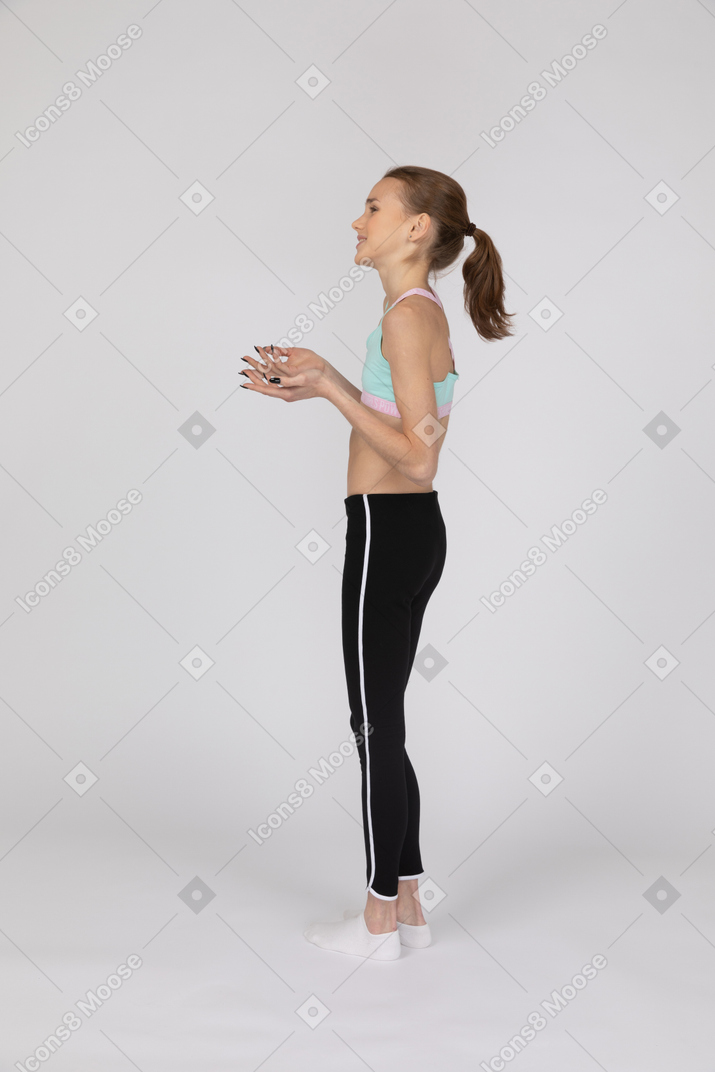 Вид сбоку девушки-подростка в спортивной одежде, которая что-то объясняет, поднимая руки