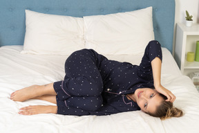 Full-length of a young lady in pajamas laying in bed and touching head