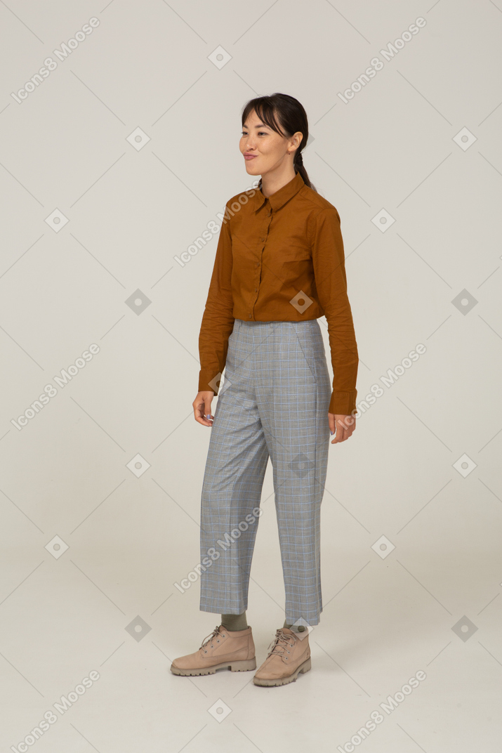 Vista de tres cuartos de una sonriente joven mujer asiática haciendo muecas en calzones y blusa