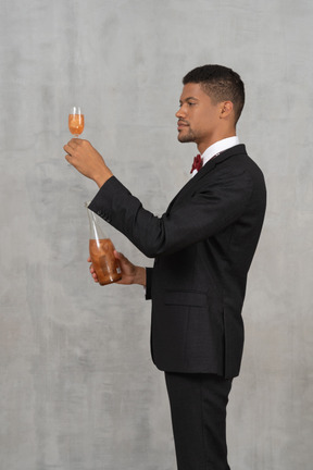 Side view of young man with a bottle raising a flute glass