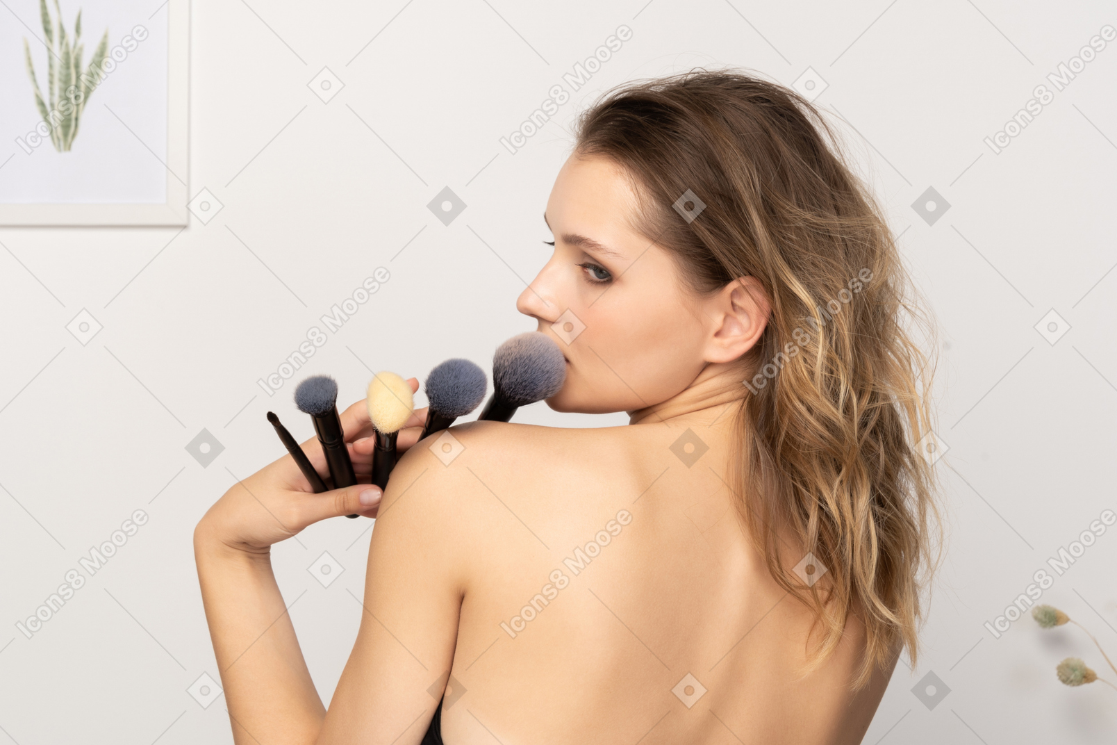 Vista posteriore di una giovane donna sensuale che tiene i pennelli per il trucco