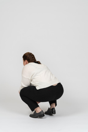 Rear view of a plump woman in casual clothes squatting