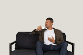 一个年轻的梦想男人坐在沙发上喝咖啡的前视图