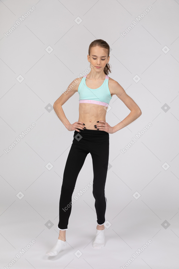 一个年轻的女孩，穿着运动服，将手放在臀部上，弯曲膝盖的前视图