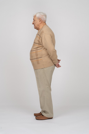 Side view of an old man in casual clothes standing with hands behind back