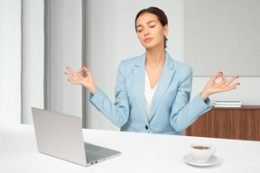 A woman sitting in yoga position at a desk in front of a laptop 