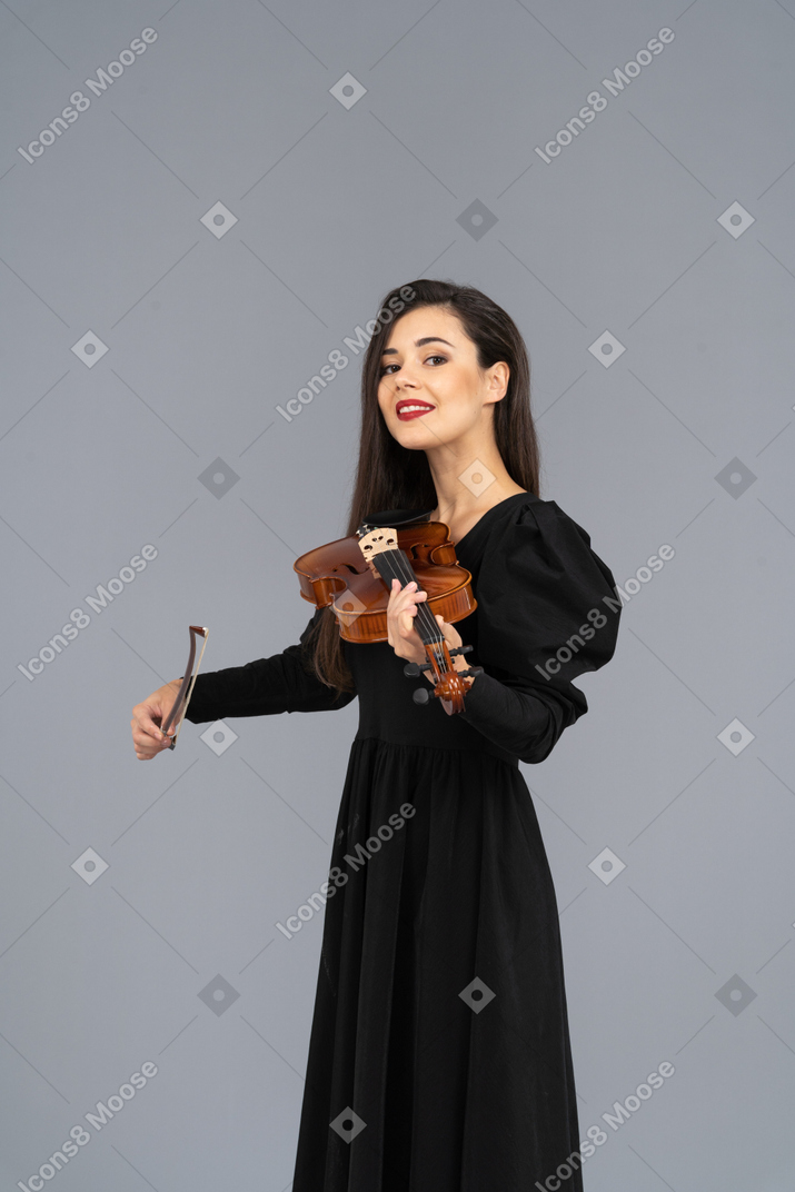 Close-up de uma jovem sorridente de vestido preto tocando violino