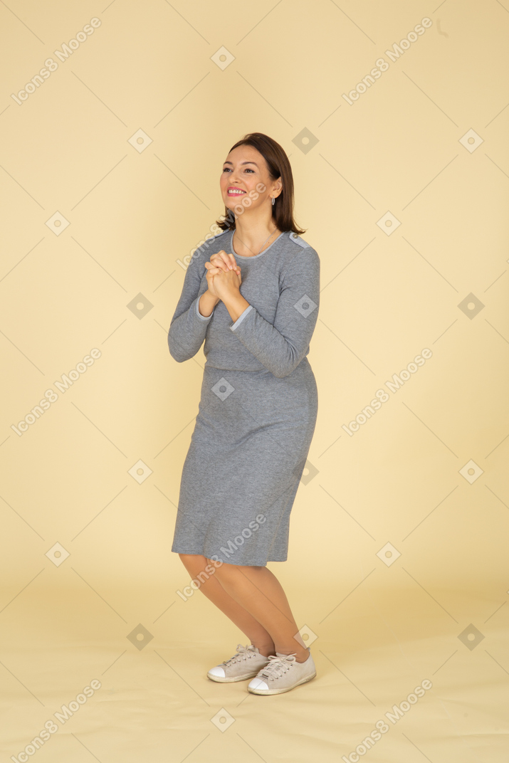 Vue de face d'une femme en robe grise faisant un geste de prière