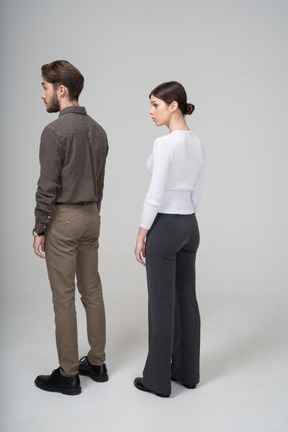 Three-quarter back view of a surprised young couple in office clothing raising brows