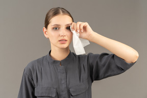 Front view of a young woman in a jumpsuit holding make up removing wipe