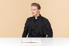 Catholic priest sitting at the table with open book on it