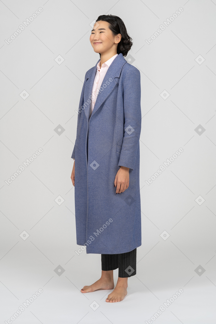 반 옆으로 서있는 긴 파란색 코트에 웃는 젊은 아시아 여자