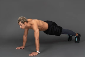 Three-quarter view of a shirtless afro man standing in plank