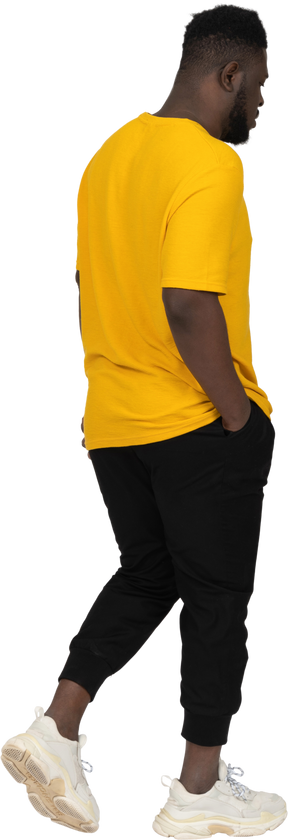 Three-quarter back view of a walking young dark-skinned man in yellow t-shirt