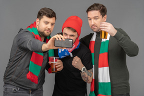 Vista frontal de tres aficionados al fútbol masculino tomando selfie