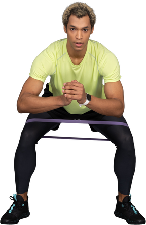 Front view of a dark-skinned young man squatting with an elastic rubber