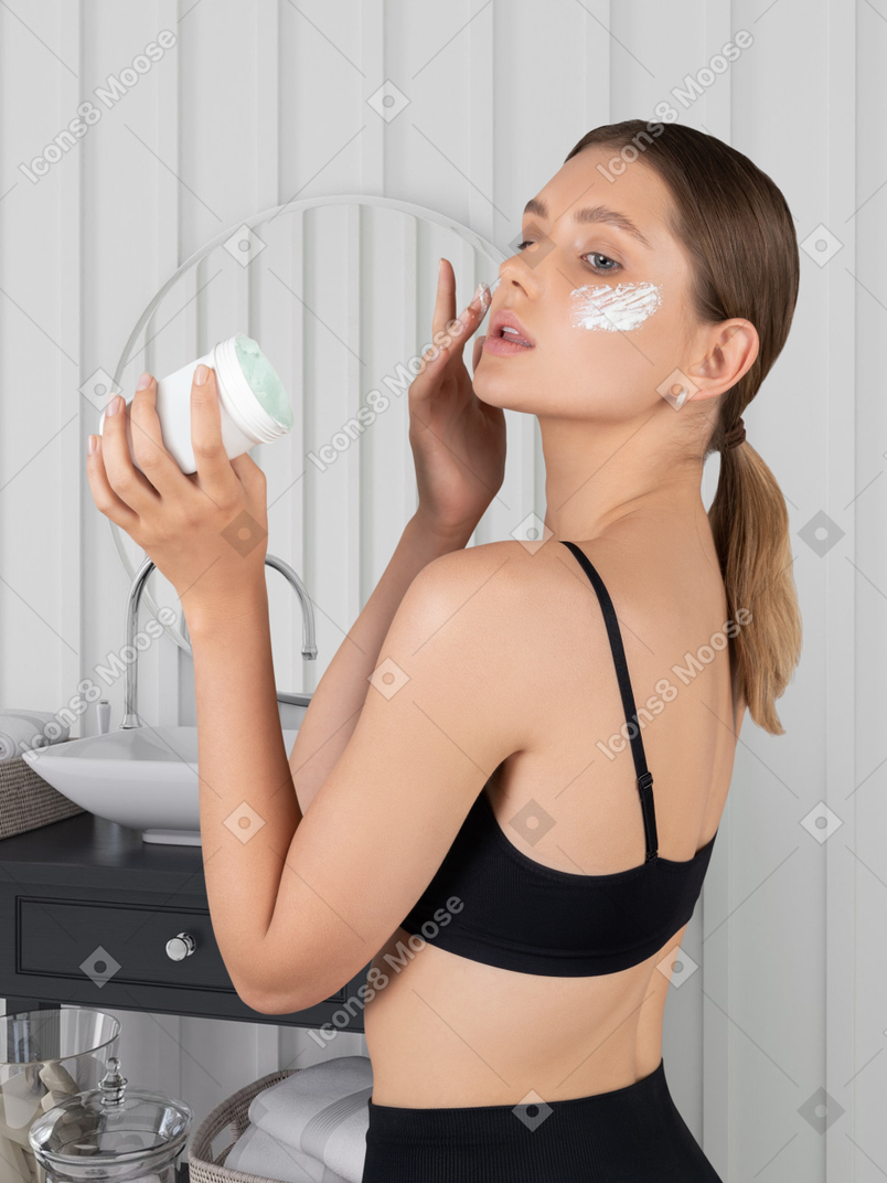 Young woman applying cream on her face