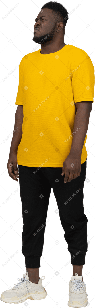 Вид в три четверти недовольного гримасничающего молодого темнокожего мужчины в желтой футболке