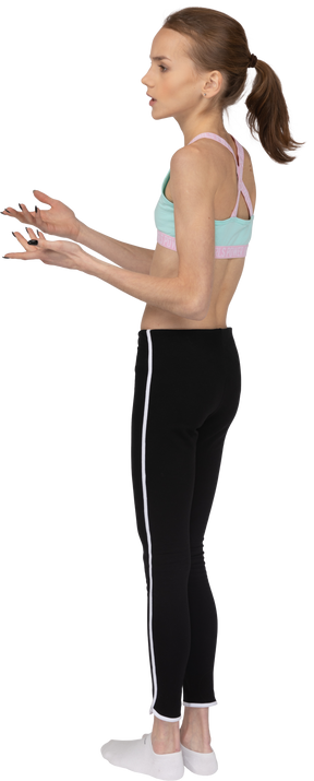 Vista posterior de tres cuartos de una jovencita en ropa deportiva levantando la mano y cuestionando