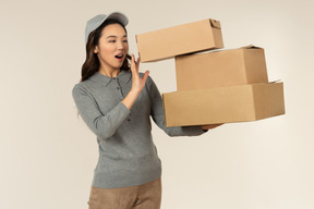 Gasping young asian delivery girl carrying boxes