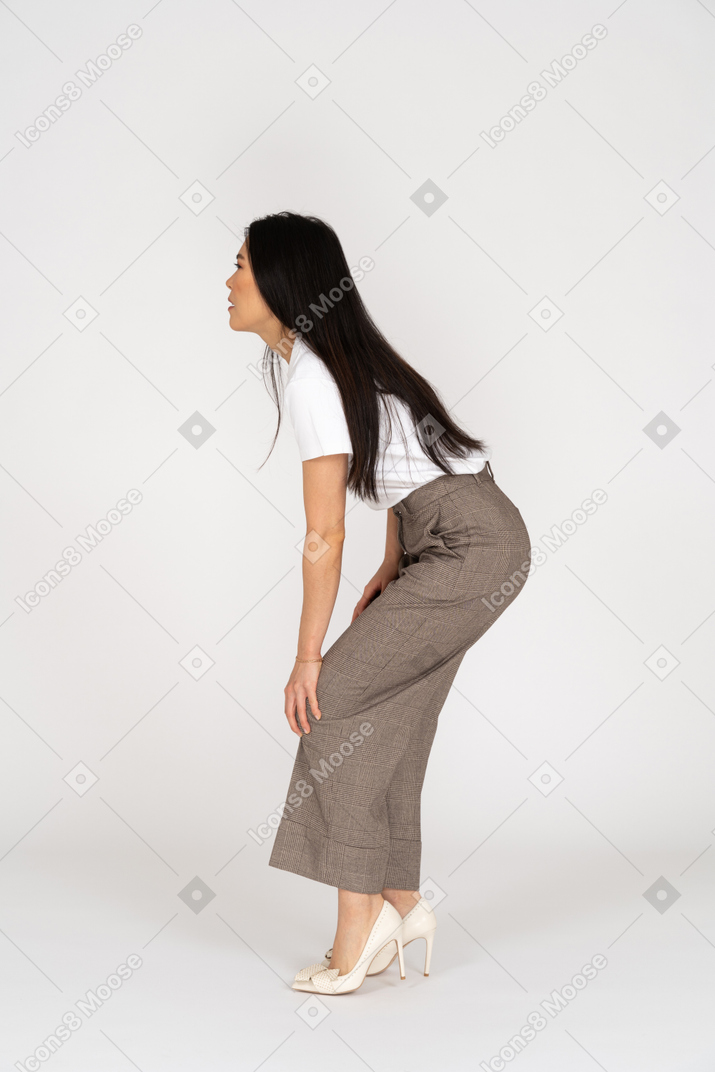 Vista lateral de uma jovem senhora de calça e camiseta inclinada para a frente