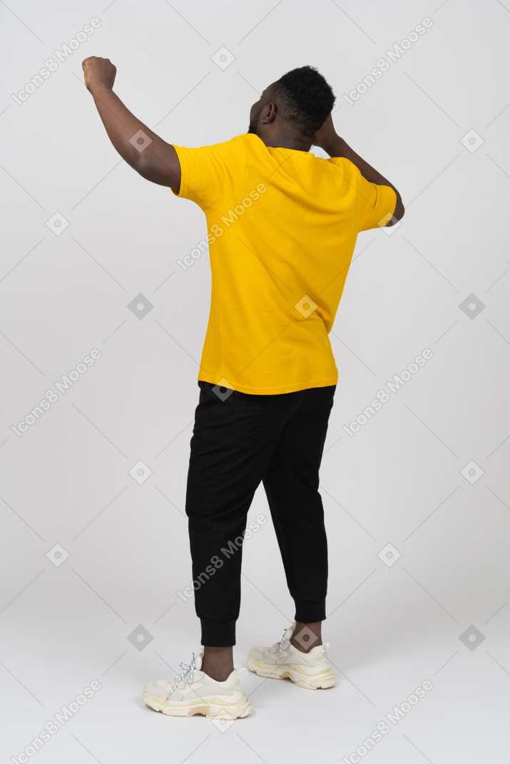 노란색 티셔츠를 입고 손을 들고 있는 행복한 젊고 어두운 피부의 3/4 뒷모습