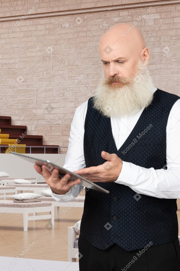 A man with a white beard is holding a tablet